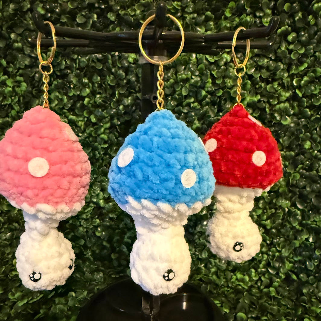 Three colorful mushroom-shaped keychains on a stand with a green leafy background.